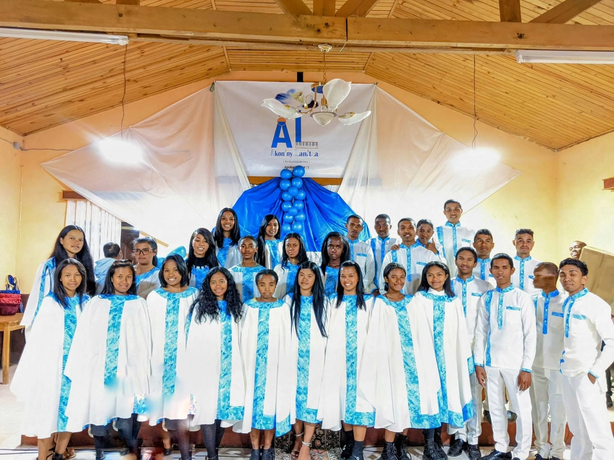 La chorale Akon'ny Lanitra en tenue blanche et bleue, devant la bannière du chœur